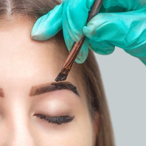 The make-up artist applies a paints eyebrow dye on the eyebrows of a young girl. Professional make-up and face care.