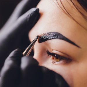 beautician- makeup artist applies paint henna on previously plucked, design, trimmed eyebrows in a beauty salon in the session correction. Professional care for face